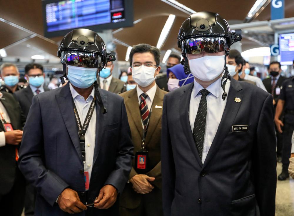 $!SMART HEADGEAR ... Transport Minister Datuk Seri Wee Ka Siong (right) and Malaysia Airport Holdings Bhd chairman Datuk Seri Zambry Abdul Kadir try out the Robocop-style helmet that can detect body temperatures, after launching the shopMYairports eCommerce platform at KL International Airport yesterday. – ASHRAF SHAMSUL/THESUN