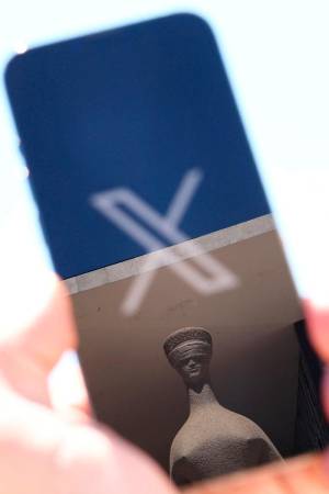 The logo of social media platform X is seen on a mobile phone next to a reflection of Alfredo Ceschiatti’s sculpture The Justice, outside Brazil’s Supreme Court in this illustration taken August 30, 2024, in Brasilia, Brazil. - REUTERSpix
