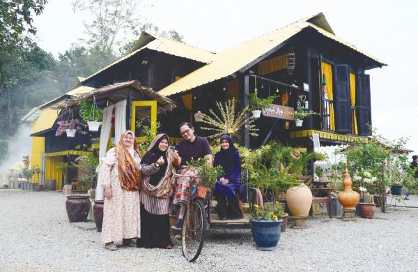 Visitor Muadz Md Nazan, 39, poses for a photo with his family in front of Rumah Atap Kuning in Bukit Lada Sayong. – BERNAMAPIX