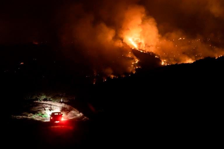 A car drives on a road in the village of Vavatsinia in the Larnaca district of Cyprus as a giant wildfire rages on the hills above during the night of July 3. — AFP