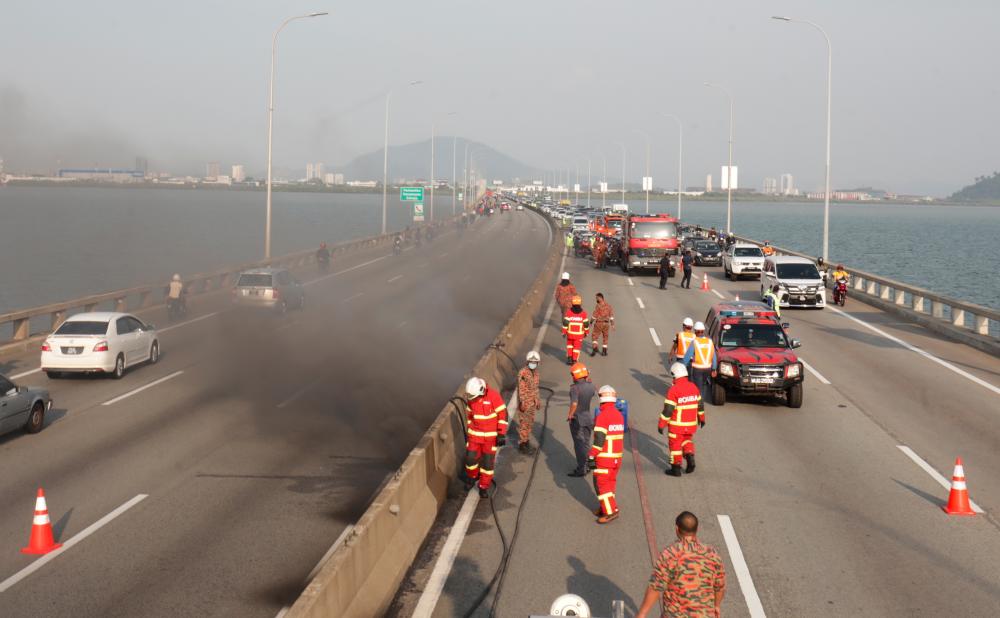 $!DANGEROUS CROSSING ... Firefighters moving in cautiously to investigate the source of smoke billowing from an electrical cable housing on the Penang Bridge yesterday. – MASRY CHR ANI/THESUN