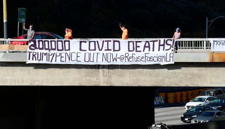 Activists unfurl a banner reading “200,000 Covid Deaths! Trump/Pence Out Now” over a freeway in Los Angeles. — AFP
