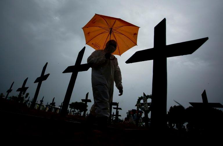 In this file photo taken on Feb 25, 2021 a worker wearing a protective suit and carrying an umbrella walks past the graves of Covid-19 victims at the Nossa Senhora Aparecida cemetery, in Manaus, Brazil. — AFP