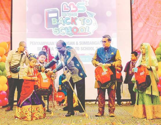 Senator Isaiah D. Jacob and Rosli presenting school bags to children at the event. – MASRY CHE ANI/THESUN