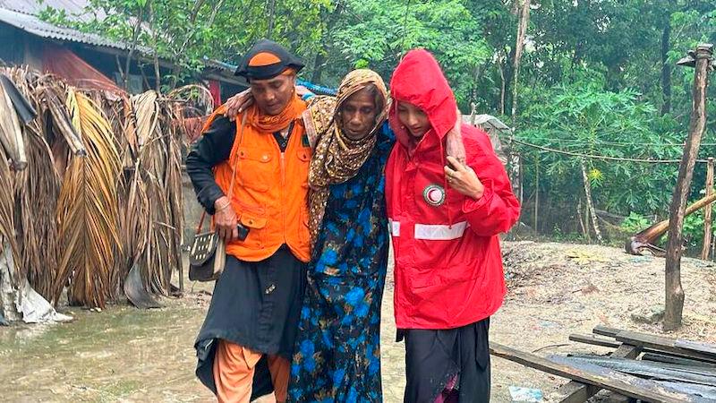 A Bangladesh Red Crescent volunteer helps a lady away from her flooded home following Cyclone Remal. The response was part funded through an IFRC-DREF allocation. - Photo: BRCS