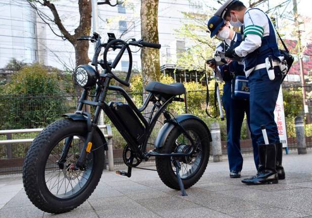 This photo taken on April 10, 2024 shows police officers checking on a bicycle along a street in the Shibuya district of central Tokyo. Cyclists using a phone in Japan could face jail time or a fine under new rules that entered into force on November 1, 2024 to tackle a rising ratio of bicycle-related accidents. - JIJI PRESS / AFP