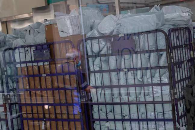 Parcels waiting to be processed are seen through a glass as a delivery worker’s reflection appears on it in a post office, as Hong Kong Post stops certain U.S.-bound shipments since April 27 due to new U.S. tariff rules, in Hong Kong, China. - REUTERS