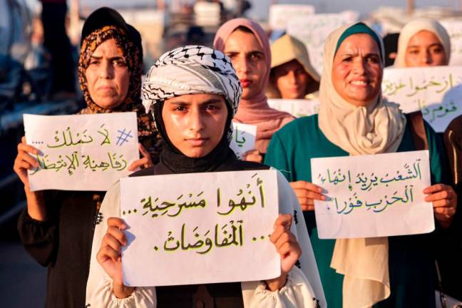 Women and children hold up signs as they attend a silent march against war and hunger in the Mawasi area in the east of Khan Yunis in the southern Gaza Strip on July 26, 2025. - AFP