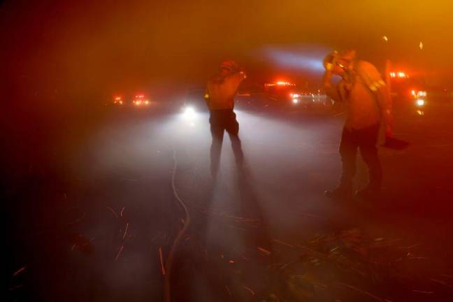 Firefighters protect themselves from strong winds through thick smoke during the Eaton Fire in Pasadena, California, U.S