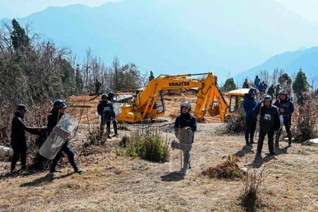 In this photograph taken on January 22, 2025, police personnel stand guard as workers use excavators at the construction site of a cable transportation system, leading to the Pathibhara Devi temple at Taplejung district, in Koshi province of Nepal. They appear tranquil when soaring above Himalayan forests, but a string of cable car projects in Nepal have sparked violent protests with locals saying environmental protection should trump tourism development. - Prakash MATHEMA / AFP