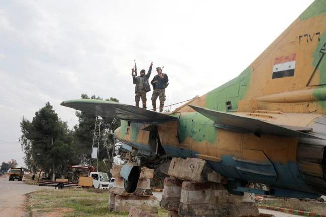 A rebel fighter gestures the victory sign while standing on a military aircraft that belonged to forces loyal to Bashar al-Assad government, inside Hama’s military airport, after Syrian rebels battled government forces for control of the key city of Homs on Saturday and advanced towards the capital Damascus as front lines collapsed across the country, throwing President Bashar al-Assad’s rule into the balance, in Hama, Syria December 7, 2024. - REUTERS/Mahmoud Hasano