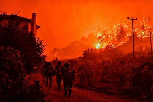 Firefighters walk on a road as a wild fire rages in the village of Ano Loutro, south of Athens, on September 30, 2024. At least two people were found dead and seven villages were evacuated due to the fire. - AFPpix