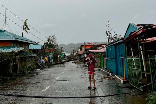 This handout taken and released on November 17, 2024 courtesy of Mayor Cesar Robles shows a resident standing past an uprooted electric post (background) in Panganiban town, Catanduanes province, after Super Typhoon Man-yi hit the province. Super Typhoon Man-yi slammed into the Philippines’ most populous island on November 17, with the national weather service warning of flooding, landslides and huge waves as the storm sweeps across the archipelago nation.