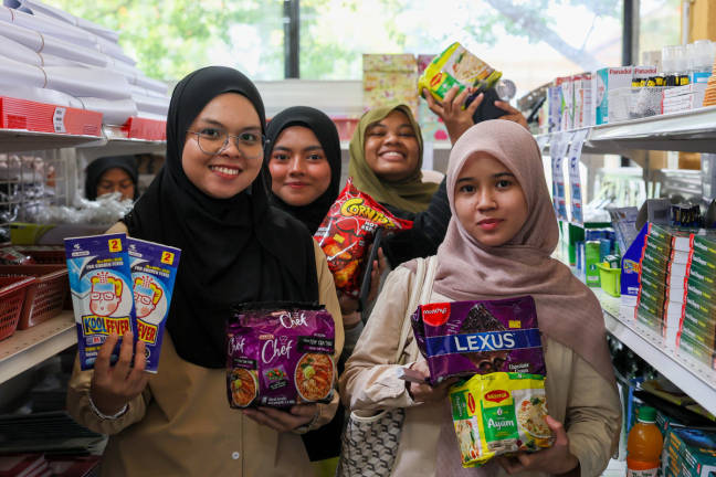 Universiti Teknologi MARA (UiTM) Dungun student Erina Natasha Mohd Saufi, 23, (left) and a friends show daily necessities purchased through the Rahmah MADANI Sales Programme (PJRM) @Campus at UiTM Dungun today. - BERNAMA