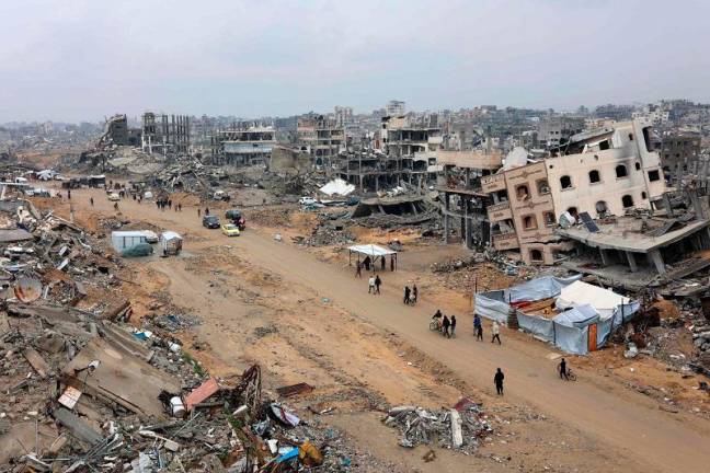 People walk amid collapsed buildings along Saftawi street in Jabalia in the northern Gaza Strip on February 5, 2025 during a ceasefire deal in the war between Israel and Hamas. Palestinian militant group Hamas lashed out on February 5, at President Donald Trump’s shock proposal for the United States to take over the Gaza Strip and resettle its people in other countries, seemingly whether they want to leave or not. - Omar AL-QATTAA / AFP