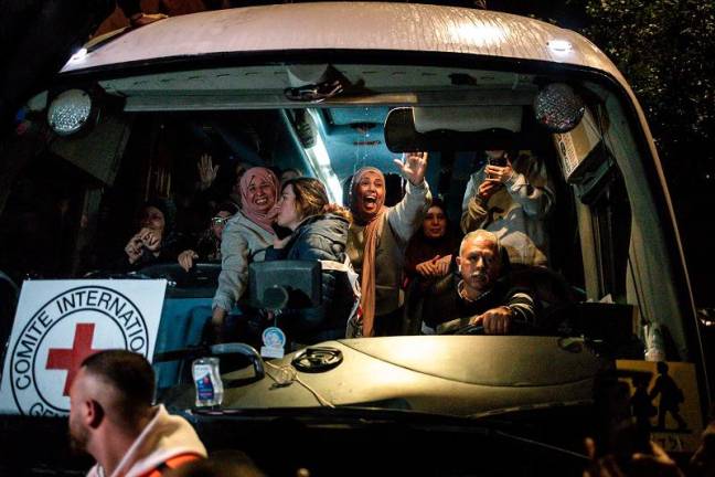 Palestinian freed prisoners wave to the crowd from a Red Cross bus that drove them out of the Israeli Ofer military prison in the occupied West Bank, as they arrive in Beitunia, on the outskirts of Ramallah, in the early hours of January 20, 2025. Crowds cheered, chanted and honked car horns as two buses carrying some 90 Palestinian prisoners freed from an Israeli jail as part of the Gaza ceasefire deal that began on January 19 and saw three Israeli hostages freed by Hamas in the Gaza Strip. - JOHN WESSELS / AFP