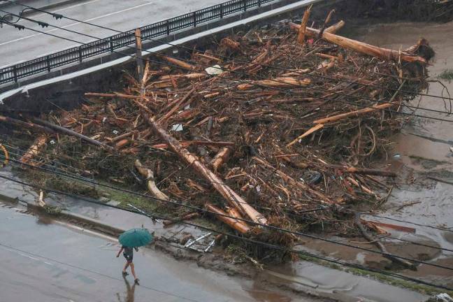 A resident walks past driftwood caught under a bridge, washed down a river after heavy rains caused flooding, in the city of Wajima, Ishikawa prefecture, on September 22, 2024. Heavy rain lashed central Japan on September 22, with floods and landslides leaving one dead and at least six missing in an area already devastated by a major earthquake this year. - JIJI PRESS / AFP