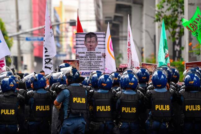 Protesters carrying a placard showing former president Rodrigo Duterte are blocked by anti-riot policemen near Malacanang palace in Manila on March 17, 2025. The protesters are calling on the government to rejoin the International Criminal Court (ICC), days after former Philippine president Rodrigo Duterte was arrested and brought to the Hague to face charges of crimes against humanity over his deadly crackdown on drugs. - TED ALJIBE / AFP