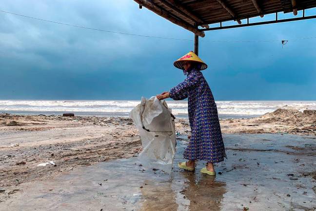 A woman wearing a raincoat collects a plastic bag near a beach as Typhoon Bualoi nears, in Nghe An province, Vietnam, September 28, 2025. - REUTERS