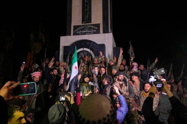 Syrian rebel fighters celebrate in front of the Clock Tower in the heart of Homs early on December 8, 2024, after entering Syria’s third city overnight. Hayat Tahrir al-Sham (HTS) and allied anti-goovernment factions have pressed a lightning offensive since November 27, sweeping swathes of the country from government control, including major cities Aleppo, Hama, Homs and the capital Damascus. - Abdulaziz KETAZ / AFP