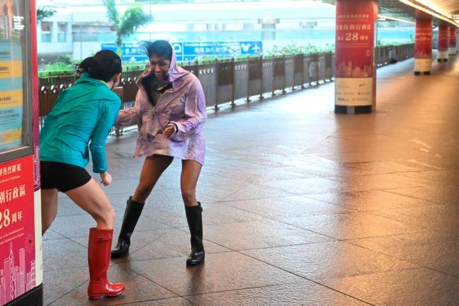 Two women brace themselves against strong winds in Central district with typhoon signal number 10 hoisted as Typhoon Wipha moves within 60km of Hong Kong on July 20, 2025. - AFP
