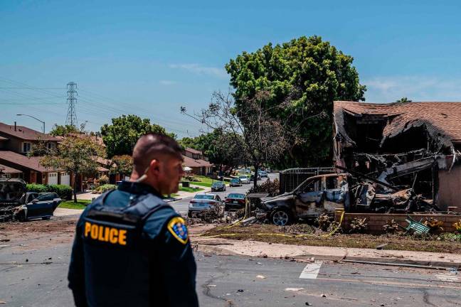 A police officer stands in front of a house that was damaged after a small plane crashed into a neighborhood, setting homes and vehicles on fire on May 22, 2025 in San Diego, California. At least two people have died after a Cessna 550 aircraft crashed into a residential street in Murphy Canyon, causing evacuations after buildings were damaged. - Ariana Drehsler/Getty Images/AFP
