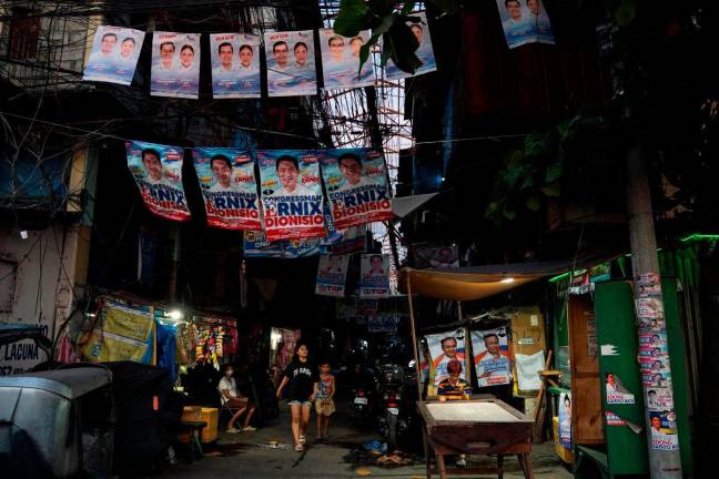 People walk past a street with campaign posters put up, a day before the May 12 midterm elections, in Manila, Philippines, May 11, 2025. REUTERS/Lisa Marie David