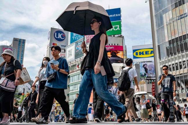 A woman uses a parasol to shelter from the sun while crossing a street in Tokyo on September 19, 2024. - Yuichi YAMAZAKI / AFP