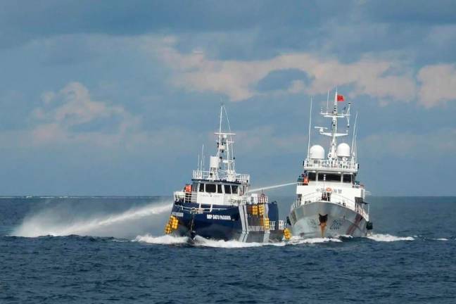 This handout photo taken and released on October 12, 2025 by the Philippine Coast Guard shows a China Coast Guard ship (R) deploying water cannon as a Philippine Bureau of Fisheries vessel (L) is seen alongside during an incident near Thitu island in disputed waters of the South China Sea. - AFP/ PHILIPPINE COAST GUARD