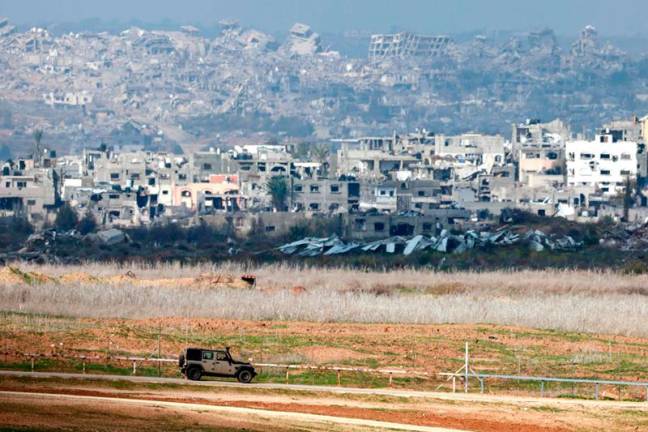 This picture taken from the Israeli side of the border with the Gaza Strip shows an Israeli army vehicle driving past destroyed buildings in the northern Gaza Strip on January 16, 2025, following the announcement of a truce amid the ongoing war between Israel and Hamas. Israel's cabinet was expected to meet on January 16, to approve a ceasefire and hostage-release deal with Hamas, Israeli media reported, a day after mediators announced an agreement they hope will lead to a permanent end to the Gaza war. - Menahem KAHANA / AFP