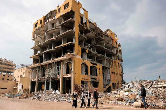 People walk past the heavily-damaged Commodore Hotel in western Gaza City, on February 11, 2025, amid the current ceasefire deal in the war between Israel and Hamas. - BASHAR TALEB / AFP