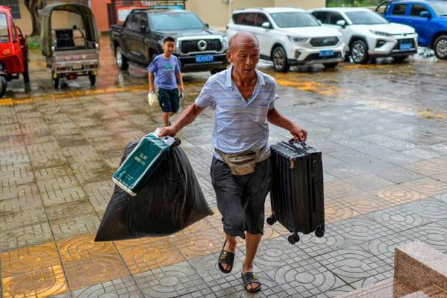 A local resident carries food and his luggage to a temporary shelter in a primary school ahead of the expected landfall of Super Typhoon Yagi in Wenchang, in southern China's Hainan province on September 6, 2024. - CNS / AFP