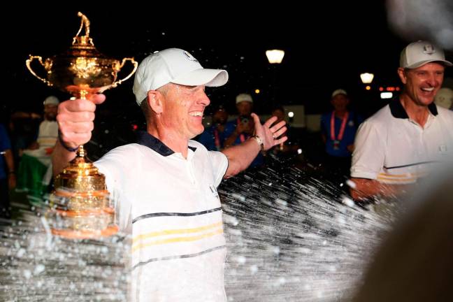 Captain Luke Donald of Team Europe holds the Ryder Cup trophy as he is doused with champagne by Rory McIlroy (not pictured) after Team Europe defeated Team United States 15-13 during the Sunday singles matches of the 2025 Ryder Cup at Black Course at Bethpage State Park Golf Course on September 28, 2025 in Farmingdale, New York. - Getty Images/AFP