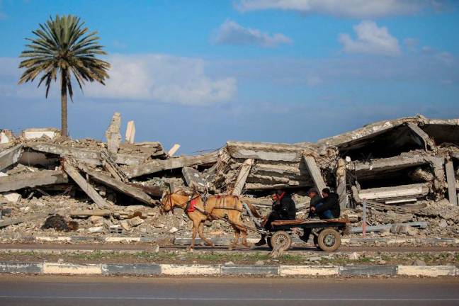 Civilians ride an animal pulled cart past the rubble of a destroyed building in al-Mughraqa in the central Gaza Strip, on February 13, 2025, as displaced people move towards the northern parts of Gaza during a current ceasefire deal in the war between Israel and Hamas. - Eyad BABA / AFP