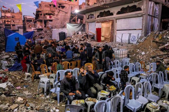 People gather for the iftar, or fast-breaking meal, on the first day of the Muslim holy fasting month of Ramadan in Jabalia in the northern Gaza Strip on March 1, 2025 by the rubble of collapsed buildings that were destroyed during the war between Israel and Hamas amid the ongoing truce. - Bashar TALEB / AFP