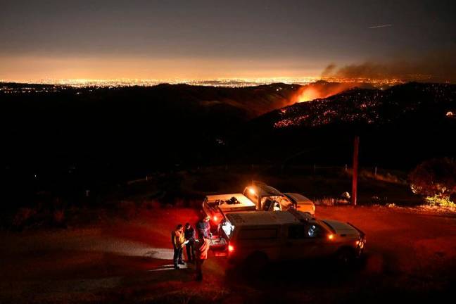 The downtown Los Angeles skyline (far L) is seen in the distance as firefighters monitor the Palisades fire near the Mandeville Canyon neighborhood and Encino, California, on January 11, 2025. The Palisades Fire, the largest of the Los Angeles fires, spread toward previously untouched neighborhoods January 11, forcing new evacuations and dimming hopes that the disaster was coming under control. Across the city, at least 16 people have died as multiple fires have ripped through residential areas since January 7, razing thousands of homes in destruction that US President Joe Biden likened to a “war scene.” - Patrick T. Fallon / AFP