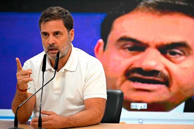 India's Congress party leader Rahul Gandhi addresses a press conference against the backdrop of a picture of Indian industrialist Gautam Adani, at his party headquarters in New Delhi on November 21, 2024. Billionaire Gautam Adani, whose business empire has been rocked by US bribery charges against him, is one of the corporate world's great survivors. - Sajjad HUSSAIN / AFP