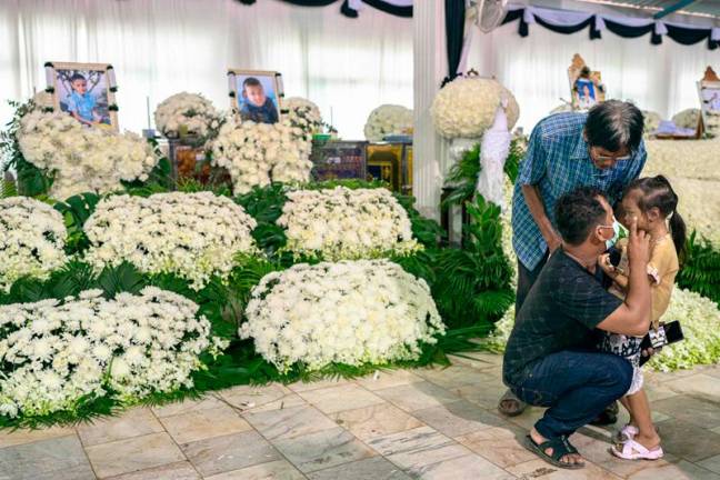 Relatives mourn in front of portraits and coffins of the victims of a school bus fire at Wat Khao Phraya Sangkharam School in Uthai Thani, on October 3, 2024. Grieving families wept as they offered prayers for 23 children and their teachers killed in a horrifying Thai school bus fire, as the government vowed a crackdown on unsafe vehicles. - AFPpix