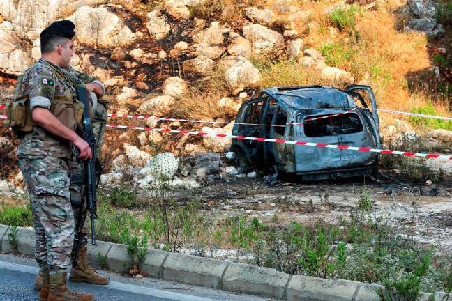 Army officers stand guard near a cordoned-off carcass of a car that was targeted in a reported Israeli drone attack in the southern Lebanese town of Al-Numairiyah on June 9, 2025. - MAHMOUD ZAYYAT / AFP