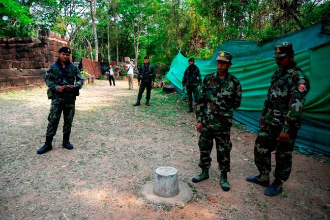 Cambodian soldiers (R) and Thai soldier (L) stand guard at the disputed ancient Khmer temple Prasat Ta Muen Thom, or Prasat Ta Moan Thom in Khmer, on the Cambodian-Thai border in Oddar Meanchey province on March 26, 2025. - AFP