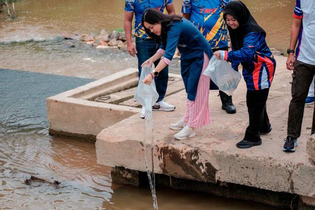 Timbalan Menteri Komunikasi Teo Nie Ching (kiri) melepaskan ikan jenis tilapia dan lampam pada Program Gotong Royong Perdana Parlimen Kulai bersempena Hari Habitat di Kampung Melayu Bukit Batu hari ini. - Bernama