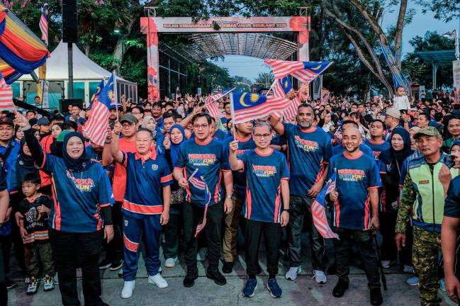 Communications Minister Datuk Fahmi Fadzil hoists the Jalur Gemilang at the Merdeka 6.8km Fun Run &amp; Walk programme in conjunction with the National Month Launch and Jalur Gemilang Flying 2025 Ceremony at Dataran Tanjung Emas, today. - Bernama pic