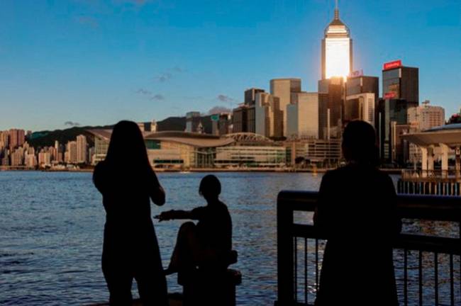 Tourists relax by the Victoria Harbour waterfront, with the iconic skyline providing a scenic backdrop, in Hong Kong on July 10, 2023. - REUTERSpix