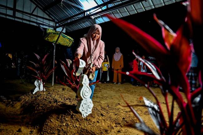 The victim’s mother, Norhasliza Yusof, 43, sprinkled rose water on the grave of her daughter, Fatin Nasrien Fadil, 22. - BERNAMApix