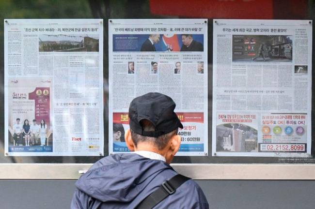 A man walks past a newspaper displayed on a street for the public in Seoul on October 21, 2024, with coverage on North Korea's decision to deploy thousands of soldiers to Ukraine's front lines and a photo (C) of North Korean leader Kim Jong Un and Russia's President Vladimir Putin toasting at a banquet in Pyongyang earlier this year. South Korea summoned the Russian ambassador to Seoul October 21 to criticise Pyongyang's decision to send thousands of soldiers, including special forces troops, to support Moscow's war in Ukraine, the foreign ministry said. - Anthony WALLACE / AFP