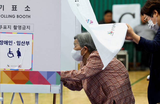 An elderly woman is assisted as she enters a booth at a polling station during the presidential election in Seoul, South Korea, June 3, 2025. - REUTERSpix