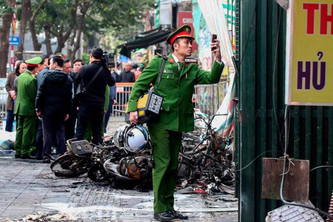 A police officer takes a photo outside the scene of a fire at a karaoke bar in Hanoi on December 19, 2024. A fire that ripped through a karaoke bar in the Vietnamese capital killed 11 people and injured two others in a suspected arson attack, police said on December 19. - Nam NGUYEN / AFP