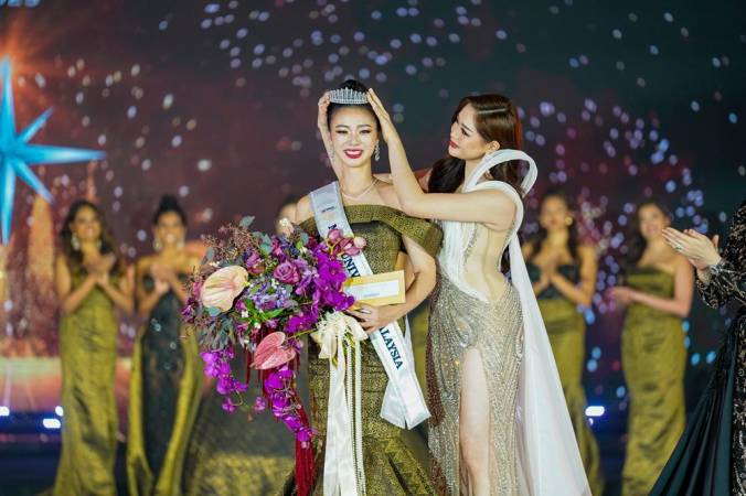 Lim (left) receives the crown for Miss Universe Malaysia 2025 from her predecessor.