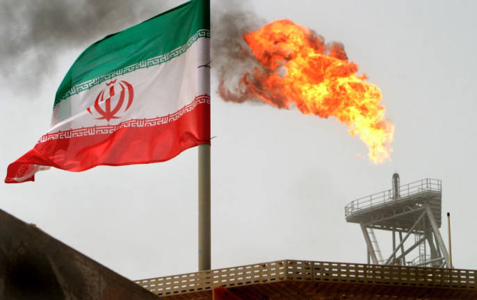 A gas flare on an oil production platform is seen alongside an Iranian flag in the Gulf July 25, 2005. - REUTERS