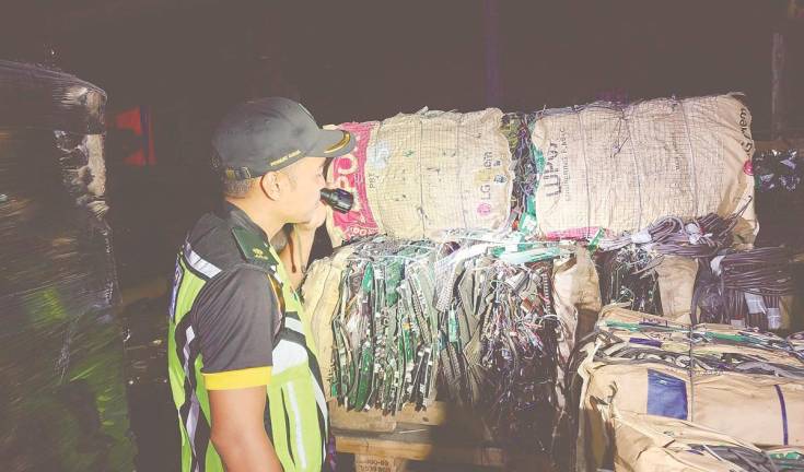 An enforcement officer examining the illegal e-waste stored at the premises. – PIC COURTESY OF Kedah Department of Environment